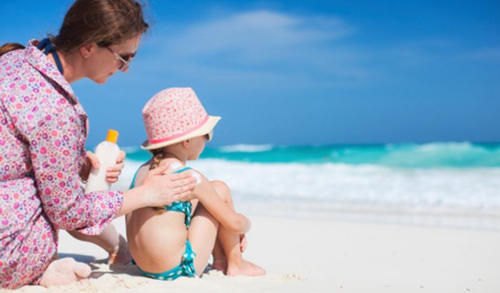 Мама наносит солнцезащитный крем ребенку на пляже